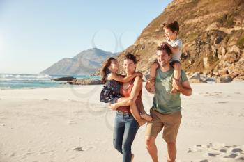 Mid adult white couple walking along on a beach carrying their children during a family holiday