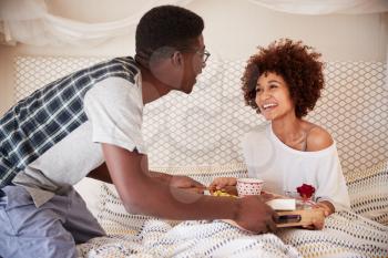 Millennial African American couple celebrating, man serving his partner breakfast in bed, close up