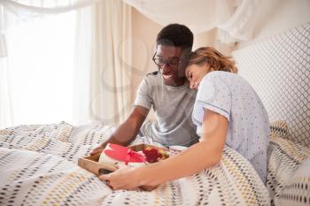 Mixed race couple embracing, man bringing his partner breakfast and gifts in bed, close up
