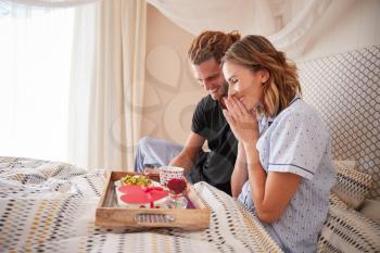 Millennial white man surprising his female partner with breakfast and gifts in bed, close up
