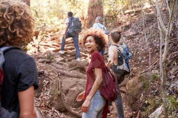 Group of millennial  friends hiking uphill on a forest trail, three quarter length