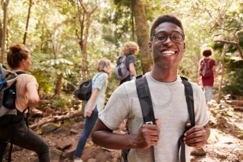 Waist up portrait of smiling millennial African American man hiking in a forest with friends, close up
