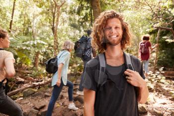 Waist up portrait of smiling millennial white man hiking in a forest with friends, close up