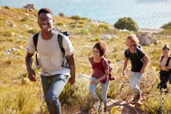 Millennial African American man leading a hike by the coast with friends, smiling to camera