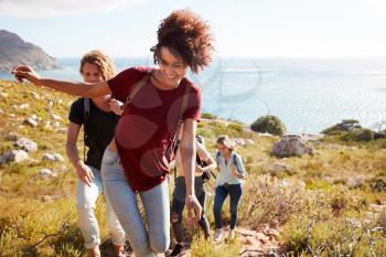 Millennial African American woman leading friends on a hike uphill by the coast, close up