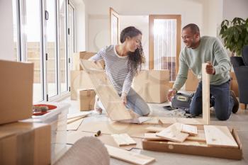 Couple In New Home On Moving Day Putting Together Self Assembly Furniture