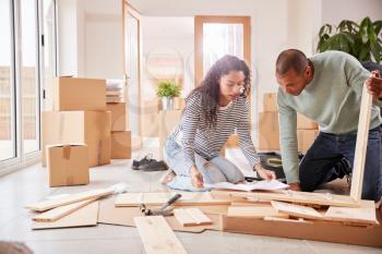 Couple In New Home On Moving Day Putting Together Self Assembly Furniture