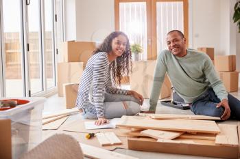 Portrait Of Couple In New Home On Moving Day Putting Together Self Assembly Furniture
