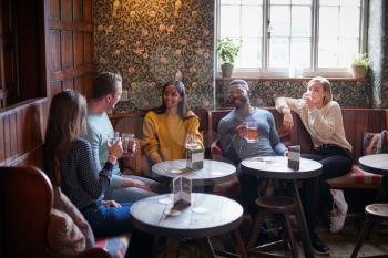 Group Of Friends Meeting For Lunchtime Drinks In Traditional English Pub