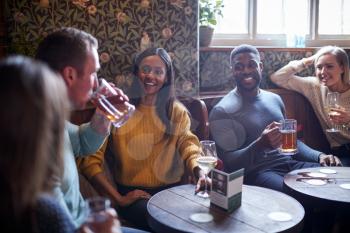 Group Of Friends Meeting For Lunchtime Drinks In Traditional English Pub