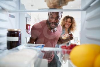 View Looking Out From Inside Of Refrigerator As Couple Open Door And Unpack Shopping Bag Of Food