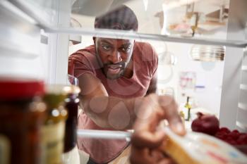 View Looking Out From Inside Of Refrigerator As Man Opens Door And Unpacks Shopping Bag Of Food