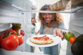 View Looking Out From Inside Of Refrigerator As Woman Opens Door For Leftover Takeaway Pizza Slice