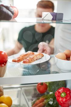 Young Man Reaching Inside Refrigerator Of Healthy Food For Fresh Salmon On Plate