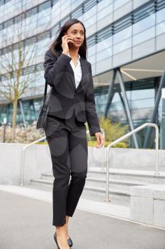 Businesswoman Commuting To Work Talking On Mobile Phone Outside Modern Office Building