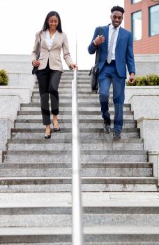 Businessman And Businesswoman Commuting To Work Walking Down Steps Outside Office Building
