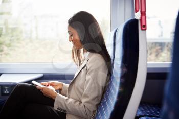 Businesswoman Sitting In Train Commuting To Work Checking Messages On Mobile Phone