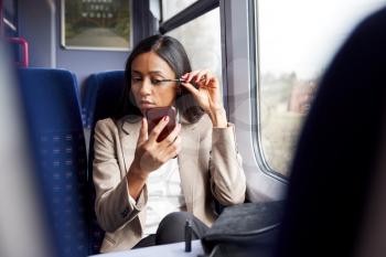 Businesswoman Sitting In Train Commuting To Work Putting On Make Up