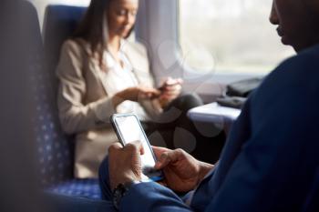 Close Up Of Business Passengers Sitting In Train Commuting To Work Looking At Mobile Phones
