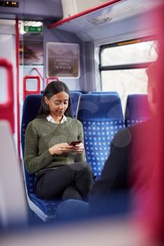 Female Passenger Sitting In Train Looking At Mobile Phone