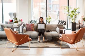 Businesswoman Sitting On Sofa Working On Laptop At Desk In Shared Workspace Office