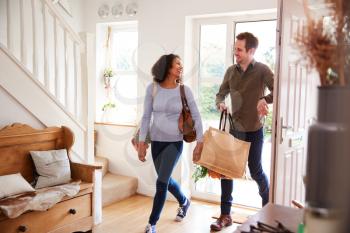 Mature Couple Returning Home From Shopping Trip Carrying Groceries In Plastic Free Bags