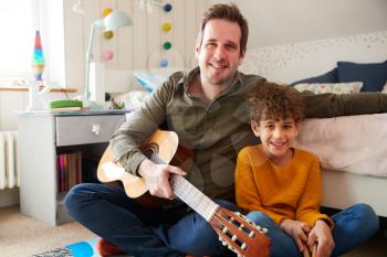 Portrait Of Single Father At Home With Son Playing Acoustic Guitar In Bedroom