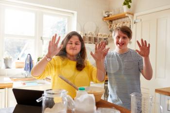 Portrait Of Downs Syndrome Couple Following Recipe On Digital Tablet To Bake Cake In Kitchen At Home