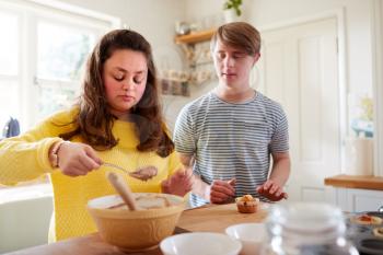Young Downs Syndrome Couple Decorating Homemade Cupcakes With Icing In Kitchen At Home