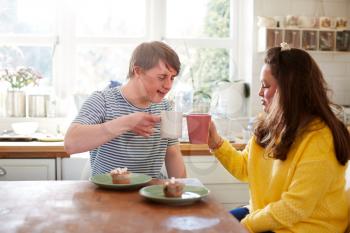 Young Downs Syndrome Couple Enjoying Tea And Cake In Kitchen At Home