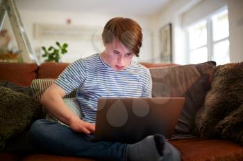 Young Downs Syndrome Man Sitting On Sofa Using Laptop At Home