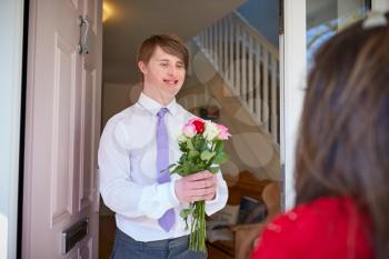 Loving Young Downs Syndrome Couple At Front Door With Man Giving Woman Flowers