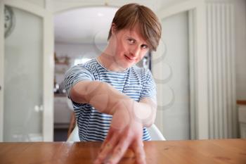 Portrait Of Young Downs Syndrome Man Sitting At Table In Kitchen