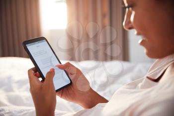 Woman Sitting Up In Bed Looking At Mobile Phone After Having Woken Up
