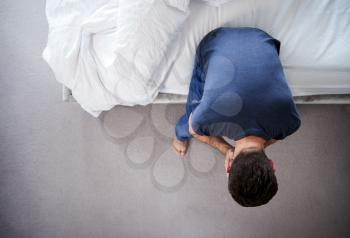 Overhead View Of Man Wearing Pajamas Suffering With Depression Sitting On Bed At Home