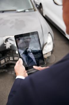 Insurance Loss Adjuster Taking Picture With Digital Tablet Of Damage To Car From Motor Accident