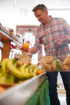 Male Customer With Shopping Basket Buying Fresh Oranges In Organic Farm Shop