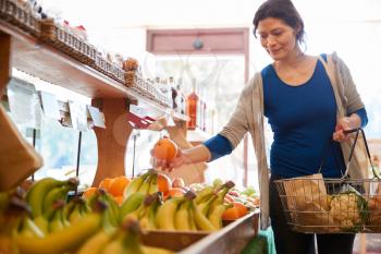 Female Customer With Shopping Basket Buying Fresh Oranges In Organic Farm Shop