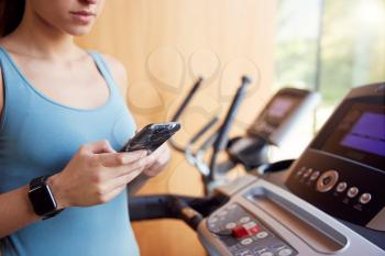 Close Up Of Woman Exercising On Treadmill Wearing Smart Watch Checking Mobile Phone