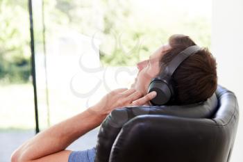 Man Relaxing In Chair At Home Listening To Music Or Podcast Music On Wireless Earphones