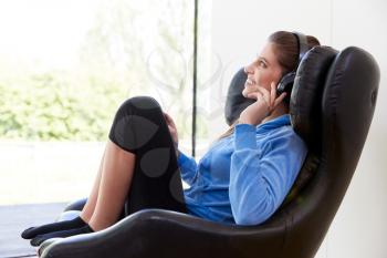 Woman Relaxing In Chair At Home Listening To Music Or Podcast Music On Wireless Earphones