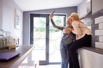 Two Female College Students Taking Selfie In Rented House Kitchen