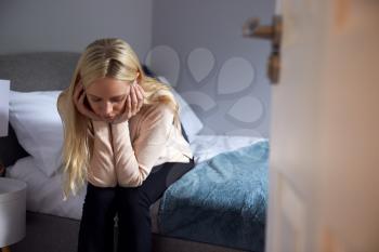 Depressed Young Woman Sitting On Bed With Head In Hands