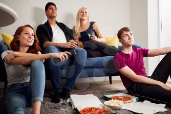 Group Of College Students In Shared House Watching TV And Eating Pizza