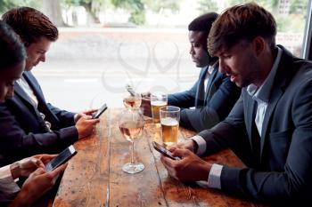 Group Of Business Colleagues All Checking Mobile Phones Whilst Meeting For Drink In Bar