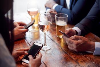 Group Of Business Colleagues All Checking Mobile Phones Whilst Meeting For Drink In Bar