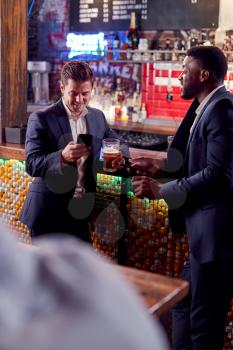 Two Businessmen Checking Mobile Phones Whilst Meeting For Drink In Bar