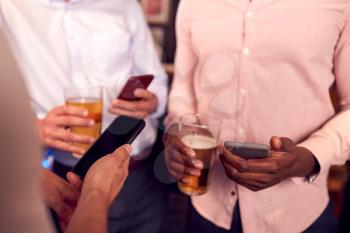 Group Of Male Friends All Checking Mobile Phones Whilst Meeting For Drink In Bar