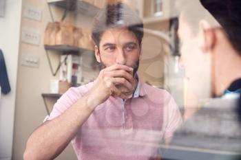 Male Gay Couple Sitting Inside Coffee Shop On Date Viewed Through Window