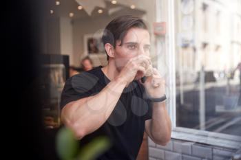 Young Man In Coffee Shop Talking On Mobile Phone Viewed Through Window